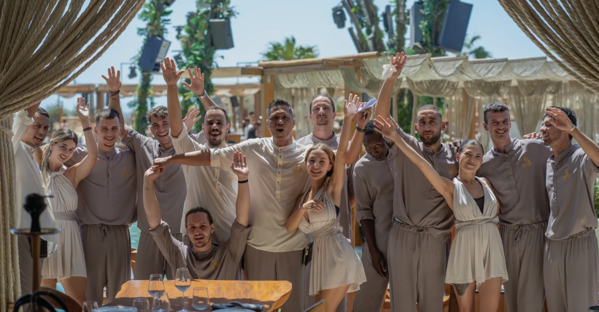 Enthusiastic SantAnna staff in neutral-toned uniforms celebrating with raised arms at the beach club.