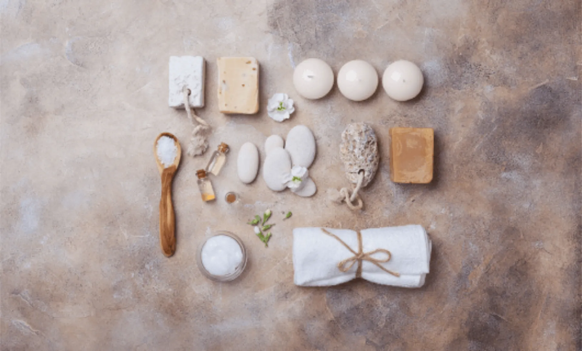 A wider view of SantAnna's beach wellness area showing a wooden deck with treatment spaces under natural canopies. The rustic structure features bamboo supports, woven roof coverings, and is surrounded by Mediterranean vegetation, with massage tables visible in the central cabana.