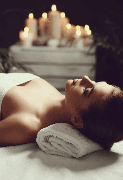 Woman relaxing during spa treatment with candles glowing softly in the background.